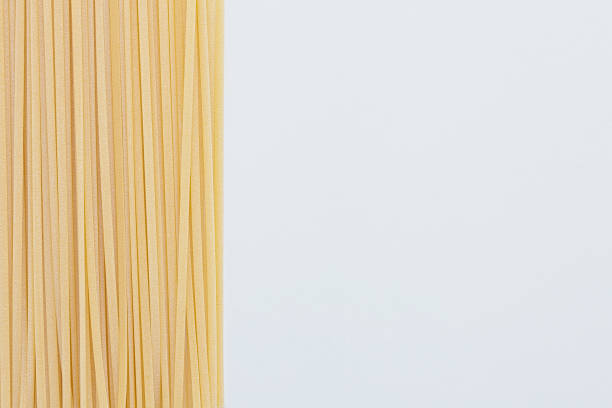 bündel von rohen linguine pasta auf der linken seite des weißen hintergrunds, kopierraum - linguini stock-fotos und bilder