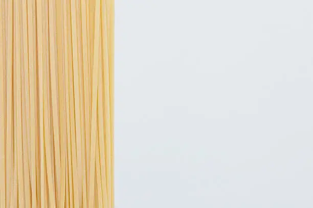 Bunch of raw linguine pasta on left side of white background, copy space