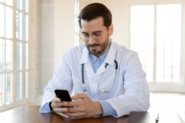 istock Focused doctor wearing glasses using smartphone, sitting at work desk 1271899026