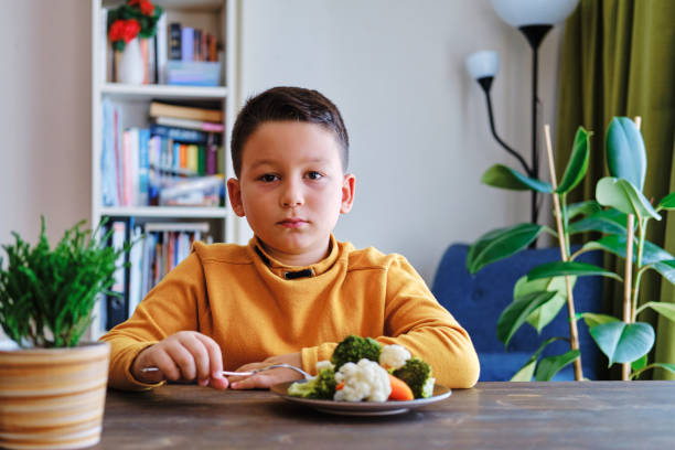 子供は野菜を食べなければならないことにとても不満を持っている。彼の皿には野菜がたくさんある。彼は野菜が嫌いだ。 - cute disgust carrot caucasian ストックフォトと画像