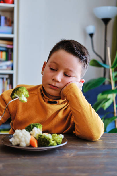 子供は野菜を食べなければならないことにとても不満です。彼の皿には野菜がたくさん載っている。彼は野菜が嫌いです。 - cute disgust carrot caucasian ストックフォトと画像