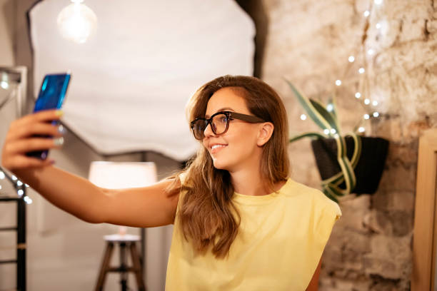 Young beautiful girl with glasses taking selfie in photography studio. stock photo