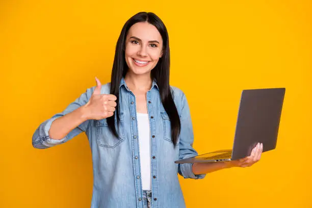 Portrait of her she nice attractive lovely pretty glad cheerful girl holding in hands laptop showing, thumbup advert ad solution isolated on bright vivid shine vibrant yellow color background