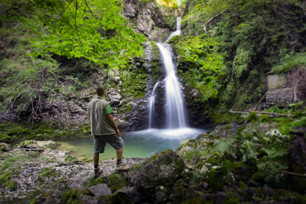 istock Young Adult Hiker Admiring Beautiful Waterfall in Wilderness 1271904865