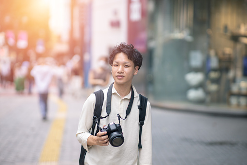 Portrait of young freelance photographer standing in city, holding digital camera