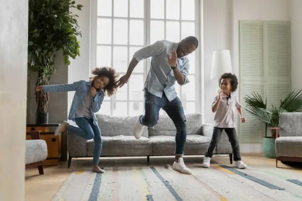 Photo of Happy african american father showing funny dancing moves to kids.