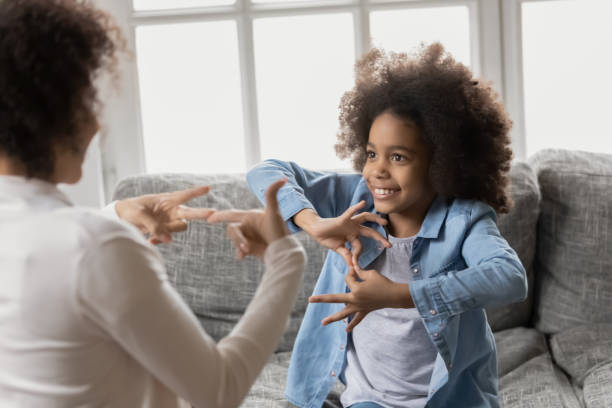 African girl with hearing loss practicing body language with therapist. Smiling little african american girl with hearing loss practicing body language with professional female therapist at home, happy deaf kid communicating nonverbal with mum using signs and gestures. deafness photos stock pictures, royalty-free photos & images