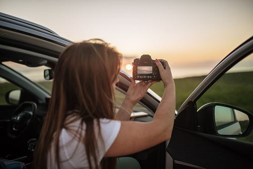 Young woman taking a photo with a DSLR camera from a car