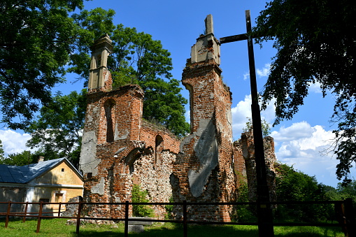 Close up on ruins of a medieval Catholic church made out of red and white bricks standing in the middle of a field overgrown with shrubs and other flora spotted on a sunny summer day in Poland