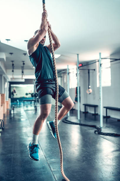 Rope Climbing Exercise By Athletic Male In Gym