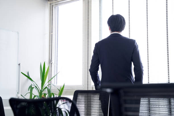 un homme d’affaires masculin japonais regardant par la fenêtre dans son bureau - rear view businessman thinking men photos et images de collection