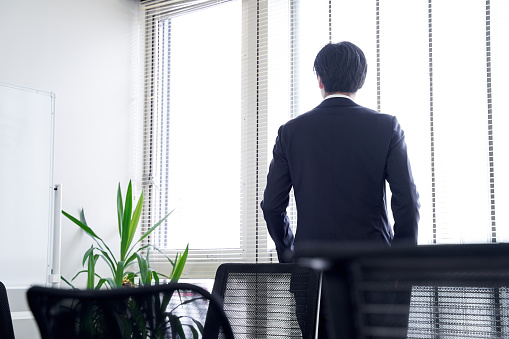 A Japanese male businessman looking out the window in his office