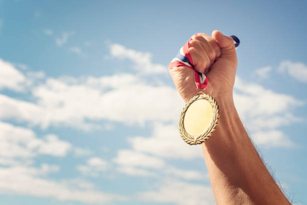 medalla de oro sostenida en mano levantada sobre fondo del cielo - medal fotografías e imágenes de stock