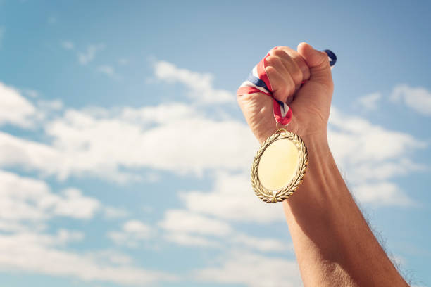 Gold medal held in hand raised against sky background Gold medal winner held in hand raised against blue sky background raised fist photos stock pictures, royalty-free photos & images