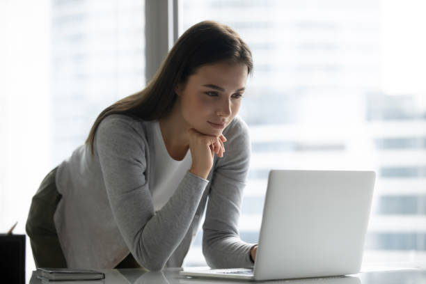 istock Focused young businesswoman standing at table in office, using laptop 1271916582