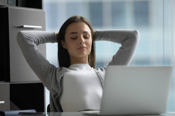Peaceful satisfied young businesswoman stretching hands, relaxing in office Peaceful satisfied young businesswoman stretching hands, leaning back in comfortable office chair, relaxing, sitting at desk, mindful woman employee resting or daydreaming, enjoying break relieved face stock pictures, royalty-free photos & images