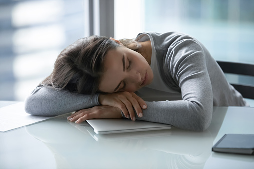 Tired exhausted young businesswoman falling asleep at work desk, suffering from lack of sleep and insomnia, overworked unmotivated woman employee student lying on table with closed eyes