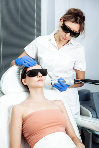 Woman Receiving Facial Beauty Treatment Removing Pigmentation At Cosmetic Clinic. Intense Pulsed Light Therapy Rejuvenation. Laser cosmetology blond doctor and patient wearing black protection glasses cuidado de la piel. mujer joven que recibe tratamiento de belleza facial, eliminando la pigmentación en la clínica cosmética. terapia de luz pulsada intensa. ipl. rejuvenecimiento, terapia facial fotográfica. procedimientos antienvejecimiento.
