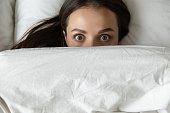 Close up top view funny young woman peeking from duvet