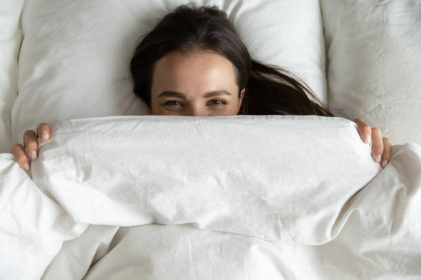 istock Top view playful cute young woman peeking from blanket 1271917079