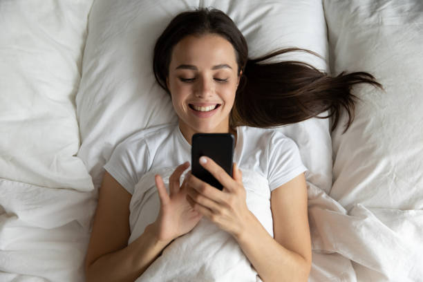 istock Top view smiling young woman using phone, relaxing in bed 1271917096
