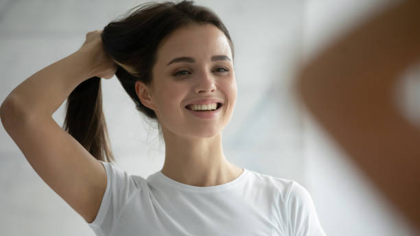 Close up head shot smiling young woman holding hairs, doing hairstyle Close up head shot smiling young woman wearing white t-shirt holding long healthy strong brown hairs, doing hairstyle, happy satisfied beautiful female standing in bathroom, looking in mirror ponytail stock pictures, royalty-free photos & images
