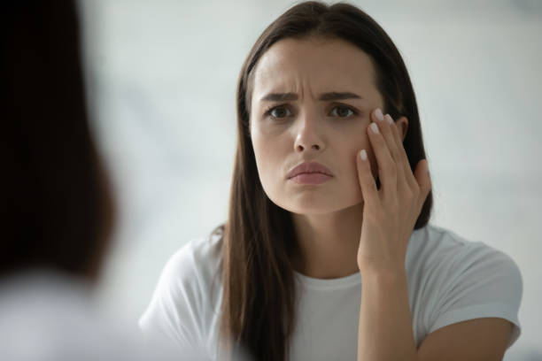 fermez la tête a tiré jeune femme malheureuse vérifiant la peau - oeil humain photos et images de collection