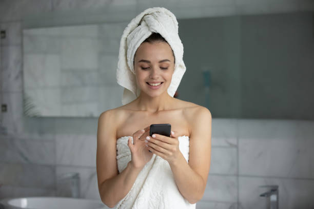 istock Smiling young woman using smartphone after shower in bathroom 1271917137