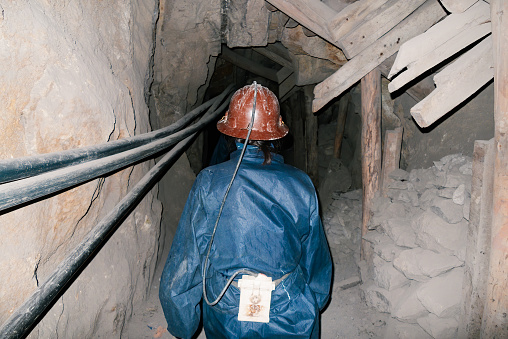 Miner with helmet and light by tunnel in silver mine, seen from behind