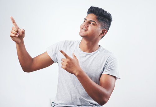 Studio shot of a young man pointing at something against a white background