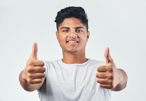 Studio shot of a young man showing thumbs up while standing against a white background