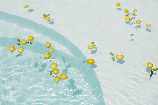 Pool Water With Citrus. Pure Aqua Surface With Glares Pattern And Floating Fresh Lemons. Clear Liquid With Sunlight Reflection In Summer.