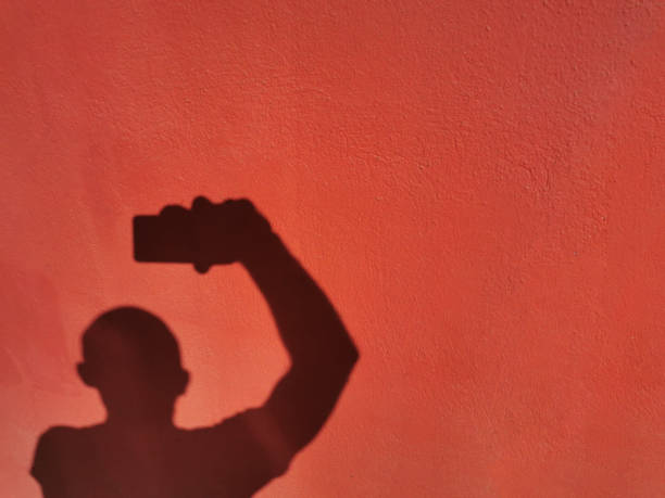 istock Shadow cast on a red wall by an anonymous person taking pictures and selfies 1271923952