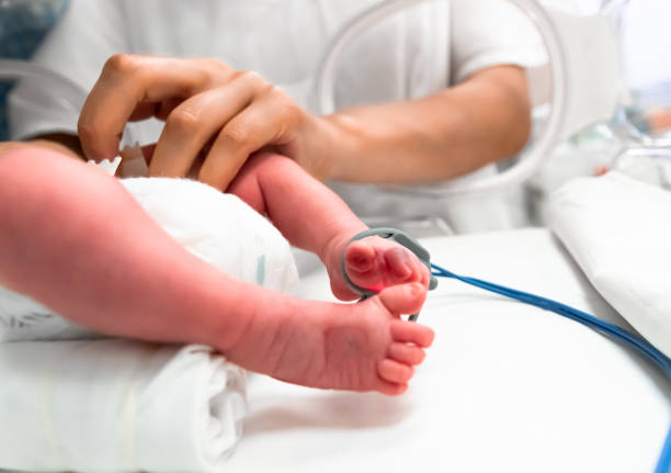 Nurse takes action to monitor and care for premature baby, selective focus - newborn baby foot with a neonatal pulse oximetry monitor and nurse arm. Newborn is placed in the incubator. Neonatal intensive care unit enfermera toma medidas para monitorear y cuidar al bebé prematuro, enfoque selectivo - pie de bebé recién nacido con un monitor de oximetría de pulso neonatal y brazo de enfermera. el recién nacido se coloca en la incubadora. unidad de cuidados intens