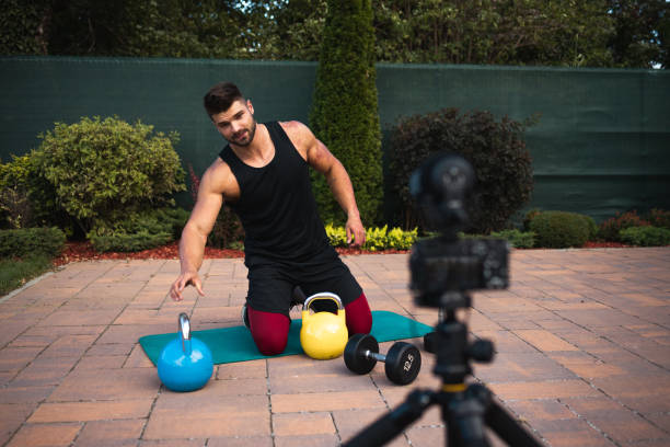 istock Male athlete sitting on exercise mat and making vlog at backyard. 1271931854