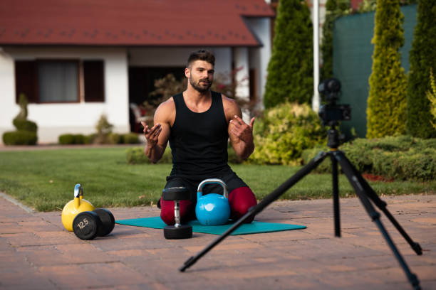 istock Male athlete sitting on exercise mat and making vlog at backyard. 1271931889