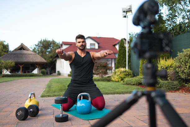 istock Male athlete sitting on exercise mat and making vlog at backyard. 1271931945