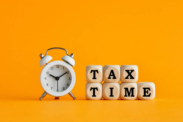 The word tax time written on wooden cubes with an alarm clock. Tax payment reminder or annual taxation concept. The word tax time written on wooden cubes with an alarm clock on yellow background. Tax payment reminder or annual taxation concept. tax season photos stock pictures, royalty-free photos & images