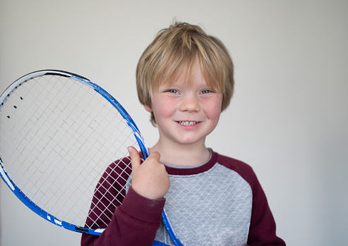 A young boy pose in front of a white screen with an old tennis racket.