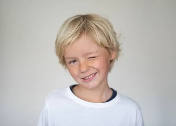 A young boy pose in front of a white screen. He is winking at the camera