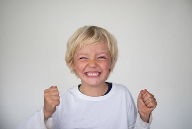 A young boy pose in front of a white screen. He is pulling a face with his fist clenched. A young boy pose in front of a white screen. He is pulling a face with his fist clenched. clenching teeth stock pictures, royalty-free photos & images