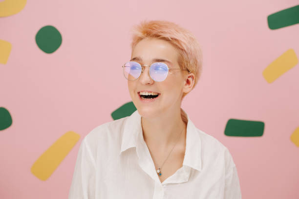 Laughing young woman with short blond hair, round glasses and stars eye makeup Laughing young woman with short dyed blond hair and round glasses and stars eye makeup. Over pink background. Looking to the side. plus size woman fashion laughing stock pictures, royalty-free photos & images