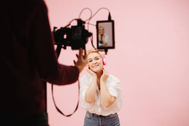 kamerzysta filmujący młodą kobietę pozującą z bezprzewodowymi słuchawkami. na różowo. - face paint audio zdjęcia i obrazy z banku zdjęć