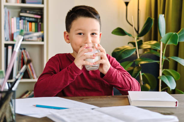 6-7 years old cute child drinking milk on table. He knows that he needs to drink milk for healthy bones. He loves milk. 6-7 years old cute child drinking milk on table. He knows that he needs to drink milk for healthy bones. He loves milk. food elementary student healthy eating schoolboy stock pictures, royalty-free photos & images