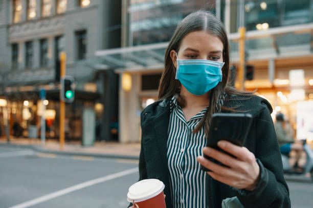 young businesswoman using smart phone with mask commuting in the business district in New Zealand young businesswoman using smart phone with mask commuting in the business district in New Zealand australasia stock pictures, royalty-free photos & images