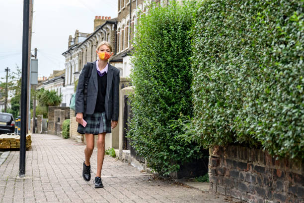 Schoolgirl walking to school wearing face mask Full length portrait of 12 year old caucasian girl walking to school in school uniform and face mask during pandemic 12 13 years pre adolescent child female blond hair stock pictures, royalty-free photos & images