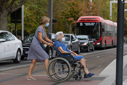 Zaragoza, Spain - August 18, 2020: Elderly woman in wheelchair wears face mask, due to the coronavirus pandemic, in the central area of Zaragoza.