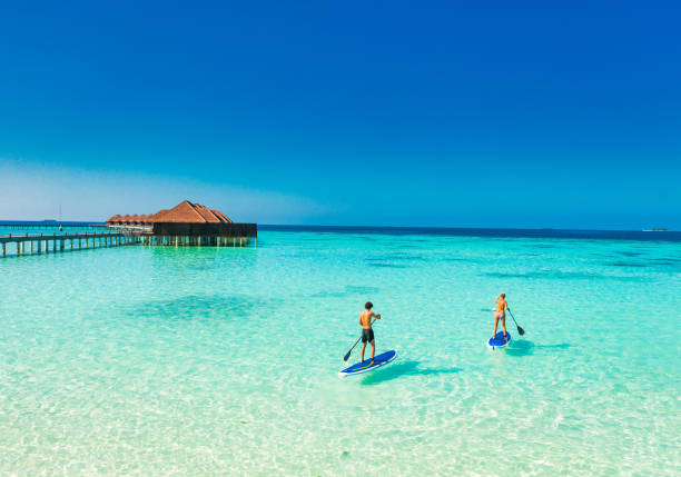 Young couple paddling on paddleboard in tropical ocean Young couple paddling on paddleboard in tropical ocean maldives stock pictures, royalty-free photos & images