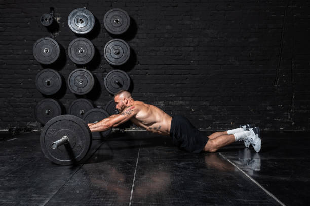 istock Young strong fit sweaty muscular man with big muscles doing abs workout by rolling barbell weights in the floor of the gym as hardcore cross training 1271951263