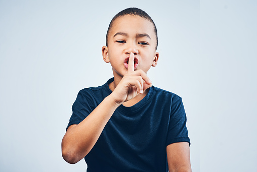 Studio shot of a cute little boy posing with his finger on his lips against a grey background